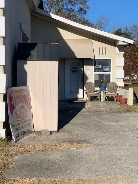The shopfront at 111 Jailhouse Alley, Byron: a stucco unit with the OPEN sign in the window, two Adirondack chairs, and the hand-painted GLASSWORKS board leaning on the wall